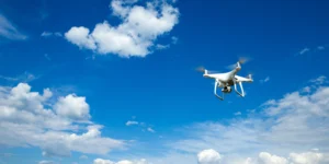 Weiße Kameradrohne fliegt bei klarem, blauem Himmel mit vereinzelten Wolken – Symbol für moderne zivile Drohnentechnologie und mobile Kommunikation aus der Luft.