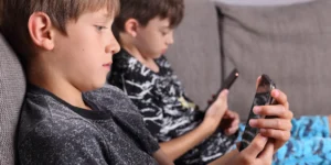 Zwei Jungen sitzen auf einem Sofa und nutzen konzentriert ihre Smartphones – Symbolbild für frühe und häufige Internetnutzung bei Kindern.