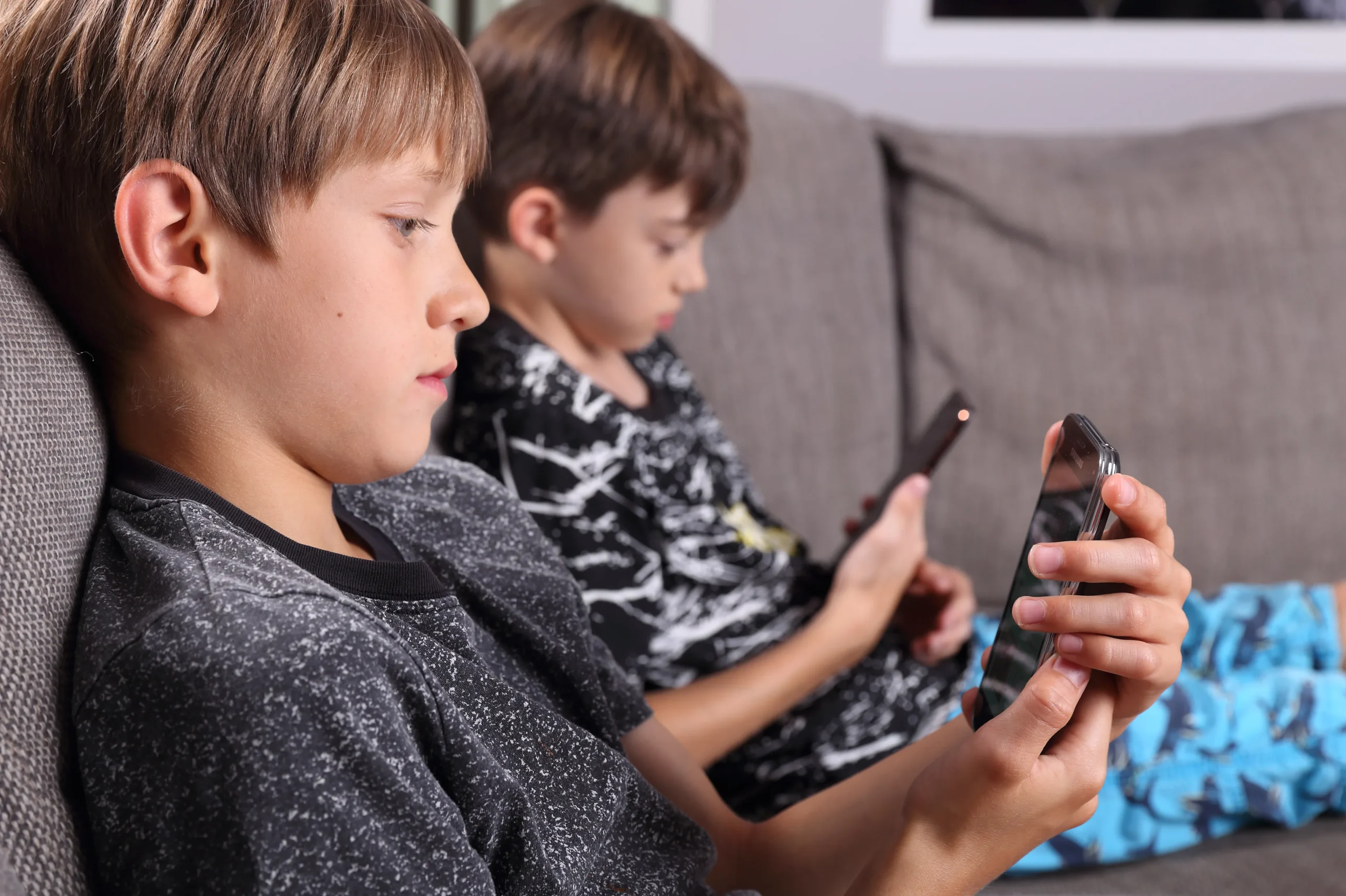 Zwei Jungen sitzen auf einem Sofa und nutzen konzentriert ihre Smartphones – Symbolbild für frühe und häufige Internetnutzung bei Kindern.