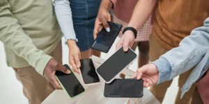 Mehrere Personen halten verschiedene Smartphones über einer offenen Box und vergleichen die Geräte.