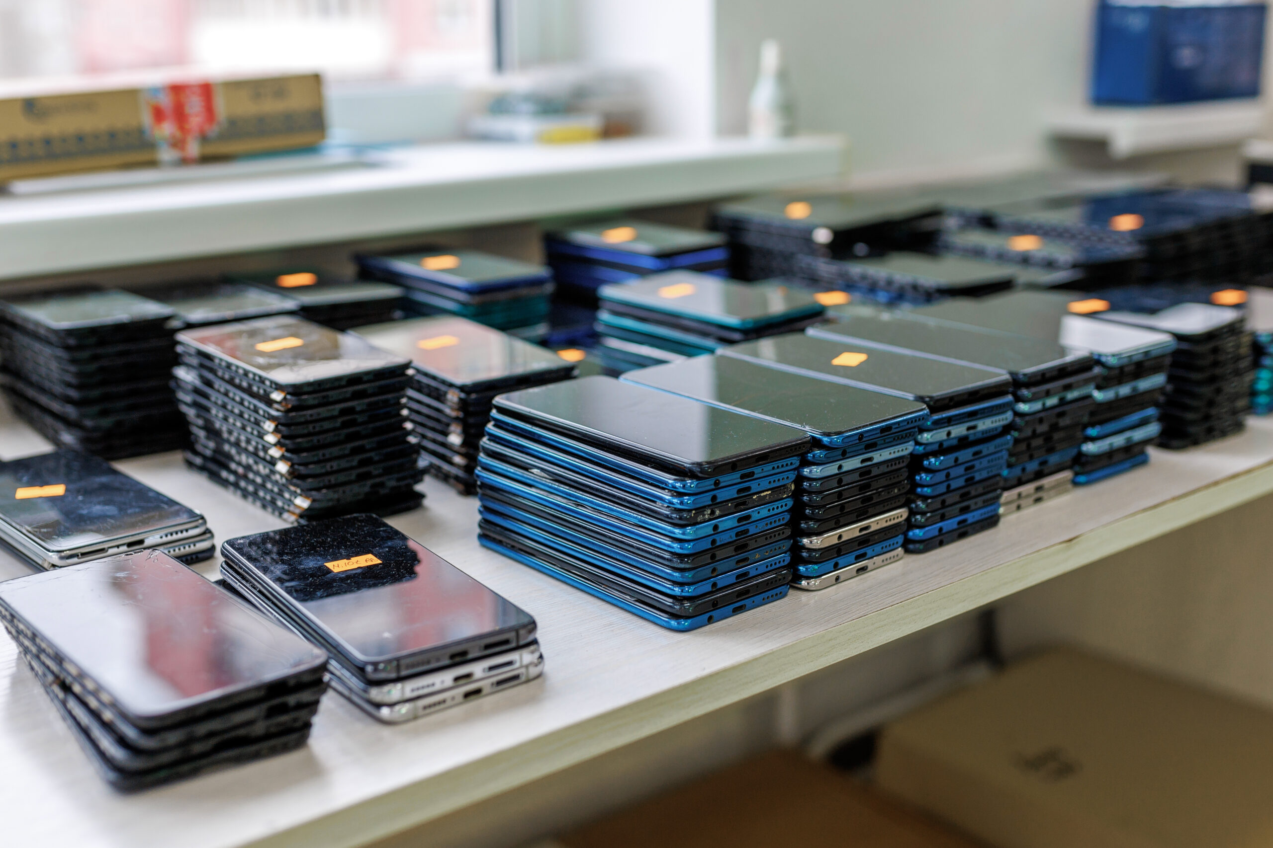 Große Menge gestapelter Smartphones auf einem Tisch in einem Techniklabor oder Reparaturbetrieb – gebrauchte und neue Mobilgeräte sorgfältig sortiert für Prüfung, Aufbereitung oder Verkauf.